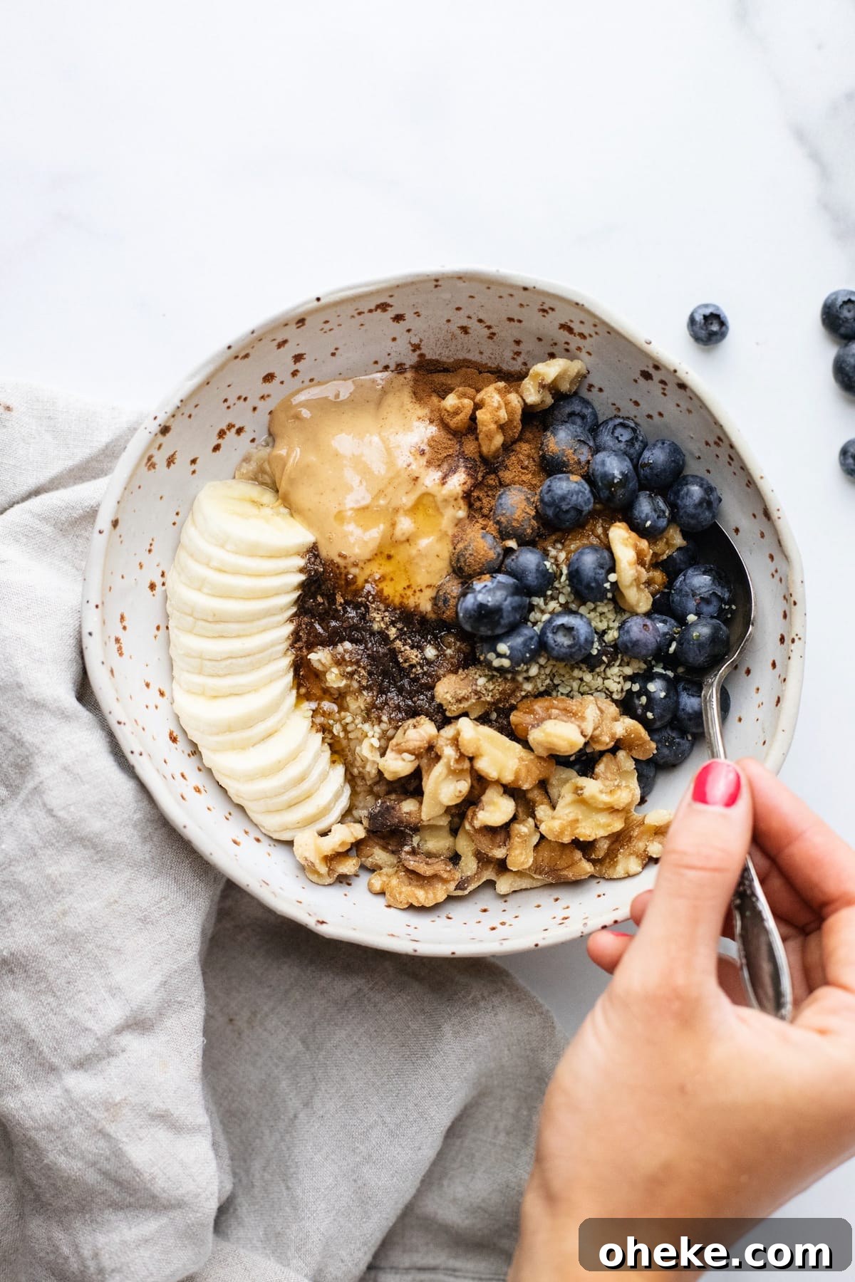 A bowl with oatmeal topped with fresh fruit and hand holding spoon.