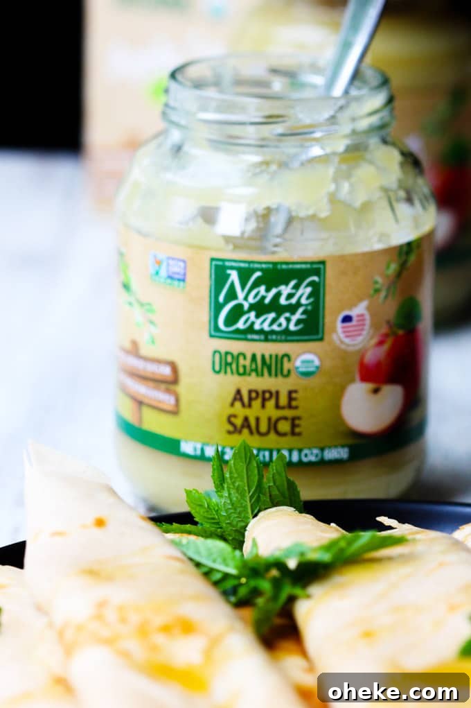These Apple Sauce Crepes with Honey Ricotta are made with cinnamon crepes, North Coast Organic Apple Sauce, organic ricotta and raw honey. These crepes are super delicious and healthy at the same time. A perfect option for a school lunch or even an afternoon snack. Apple sauce in a jar with a spoon and crepes on a plate