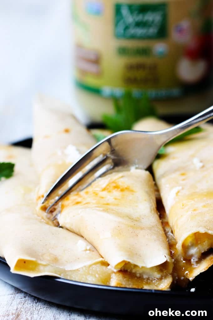 These Apple Sauce Crepes with Honey Ricotta are made with cinnamon crepes, North Coast Organic Apple Sauce, organic ricotta and raw honey. These crepes are super delicious and healthy at the same time. A perfect option for a school lunch or even an afternoon snack. Fork cutting through Apple Sauce Crepe