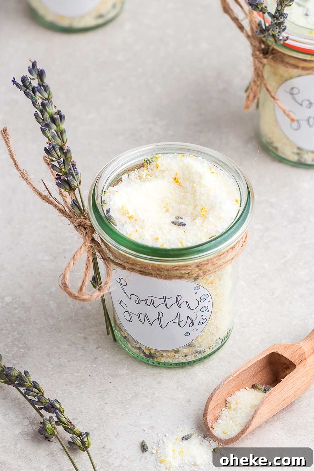 A jar of lavender salt with a wooden spoon next to it, perfect for a homemade bath salts gift jar.
