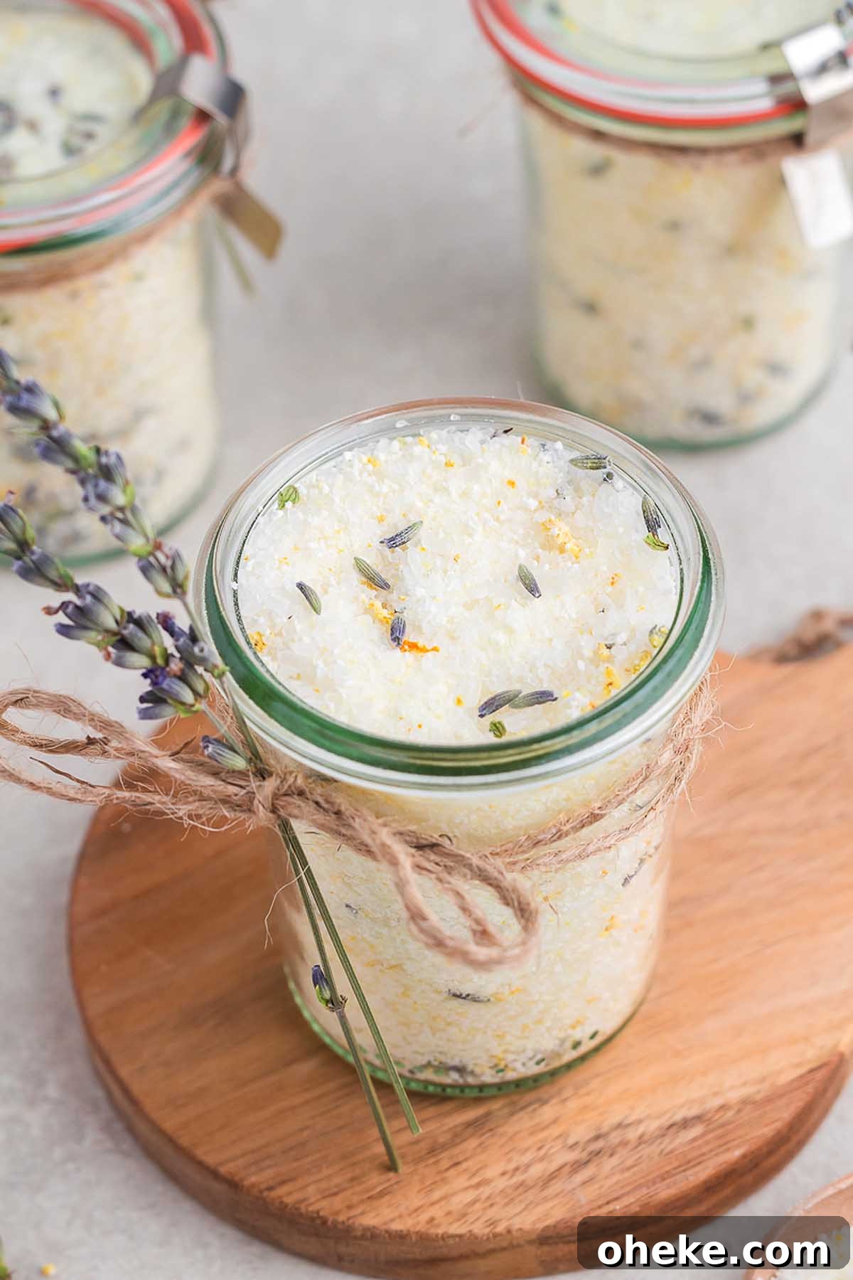 Homemade lavender bath salts displayed in beautiful jars on a rustic wooden cutting board.