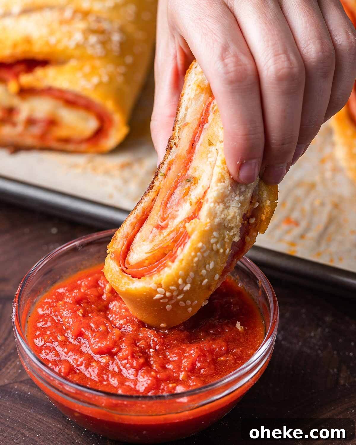 Hands dipping stromboli in marinara sauce.
