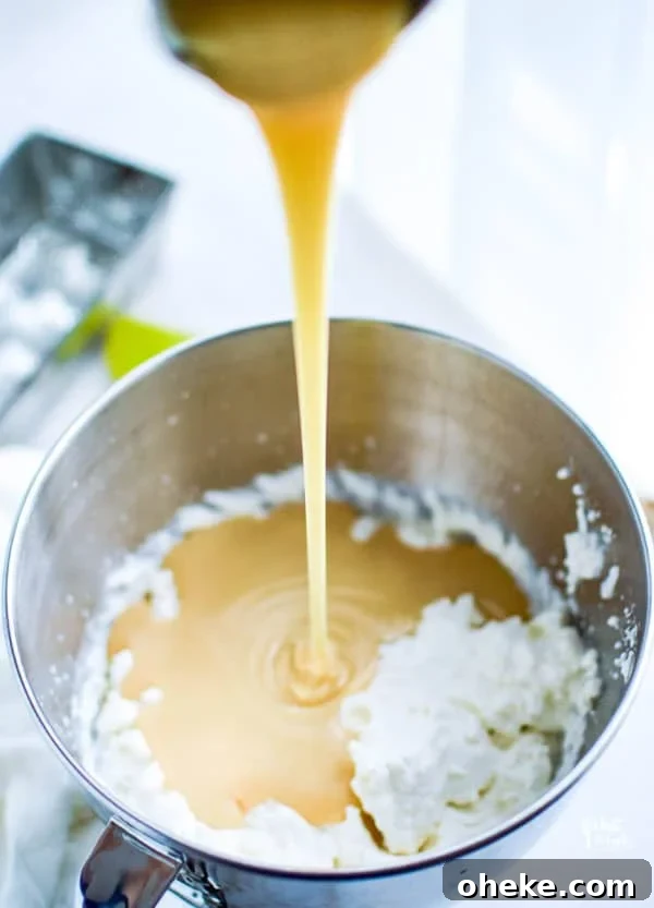 sweetened condensed milk being poured into a bowl of whipped cream to make no churn homemade vanilla ice cream