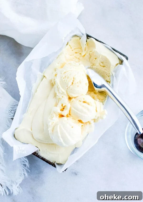 overhead shot of homemade vanilla ice cream in a silver loaf pan lined with white parchment paper that has started to be scooped