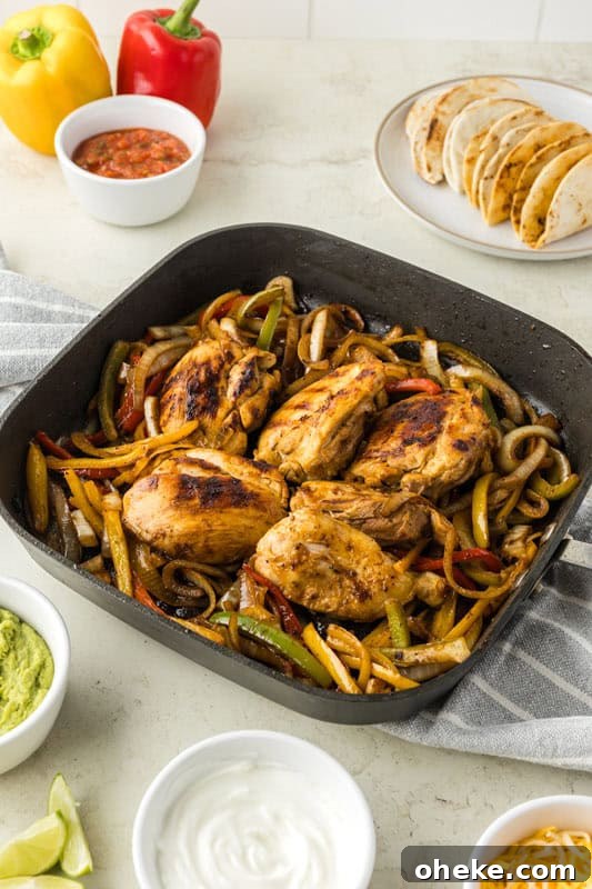 A skillet with cooked chicken breasts and mixed bell peppers is on a counter with small bowls of salsa, guacamole, sour cream, shredded cheese, and a plate of sliced tortillas ready for making delicious chicken fajita tacos.