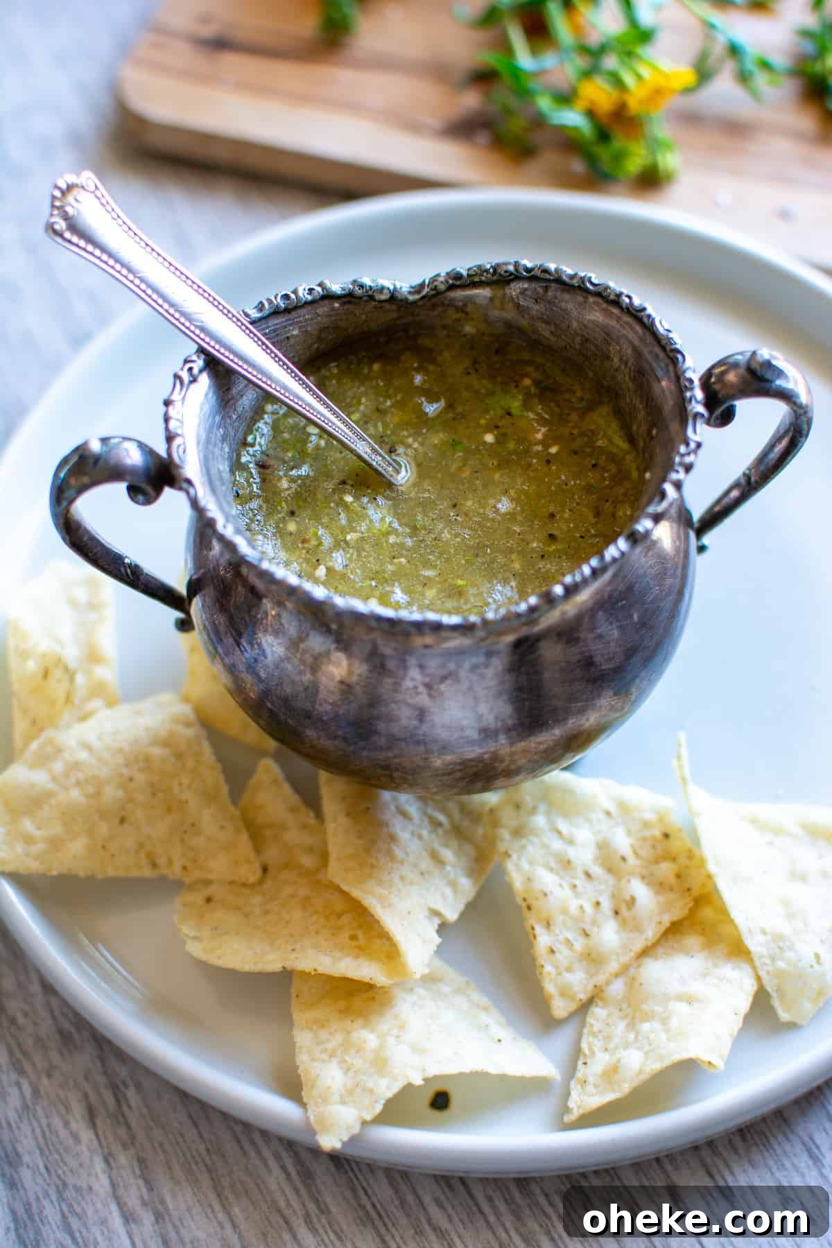 A metal serving bowl filled with habanero salsa with a spoon sticking out of one side. The bowl is sitting on a plate.