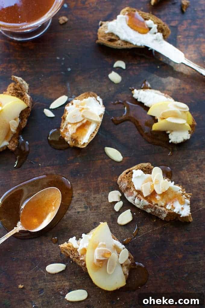 Several toasts smeared with goat cheese and topped with slices of pear, sliced almonds and honey on a wood table.