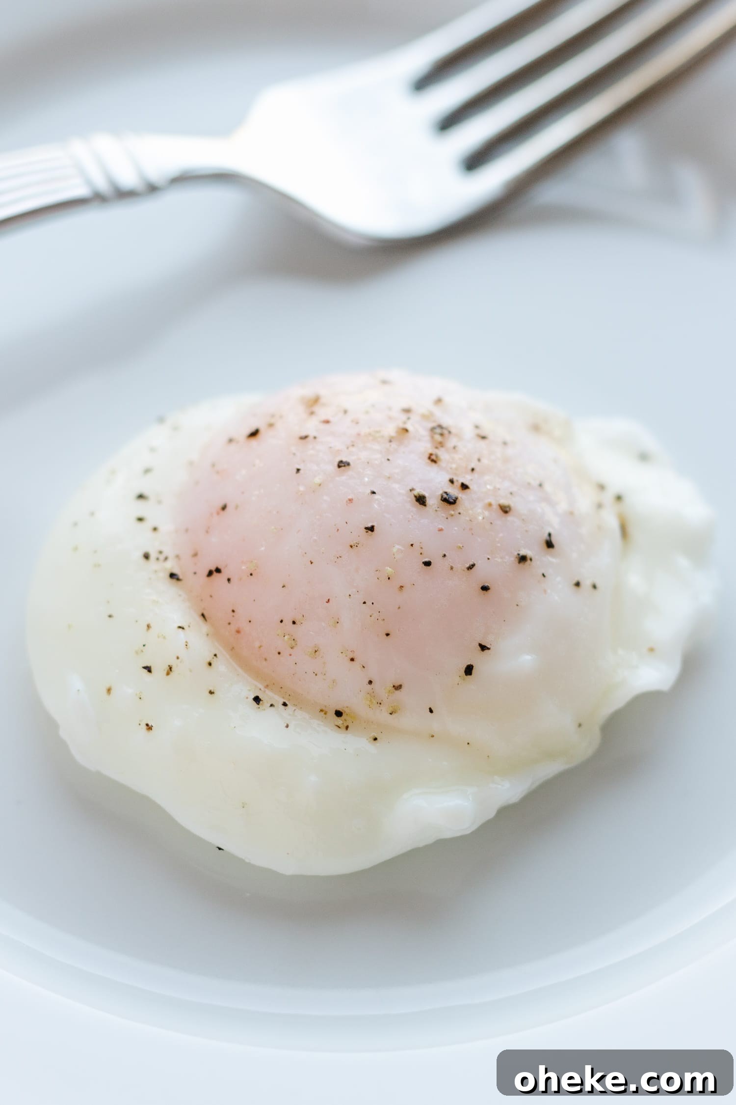 A poached egg on a white plate with a fork that has cut in to release some of the oozy yolk.