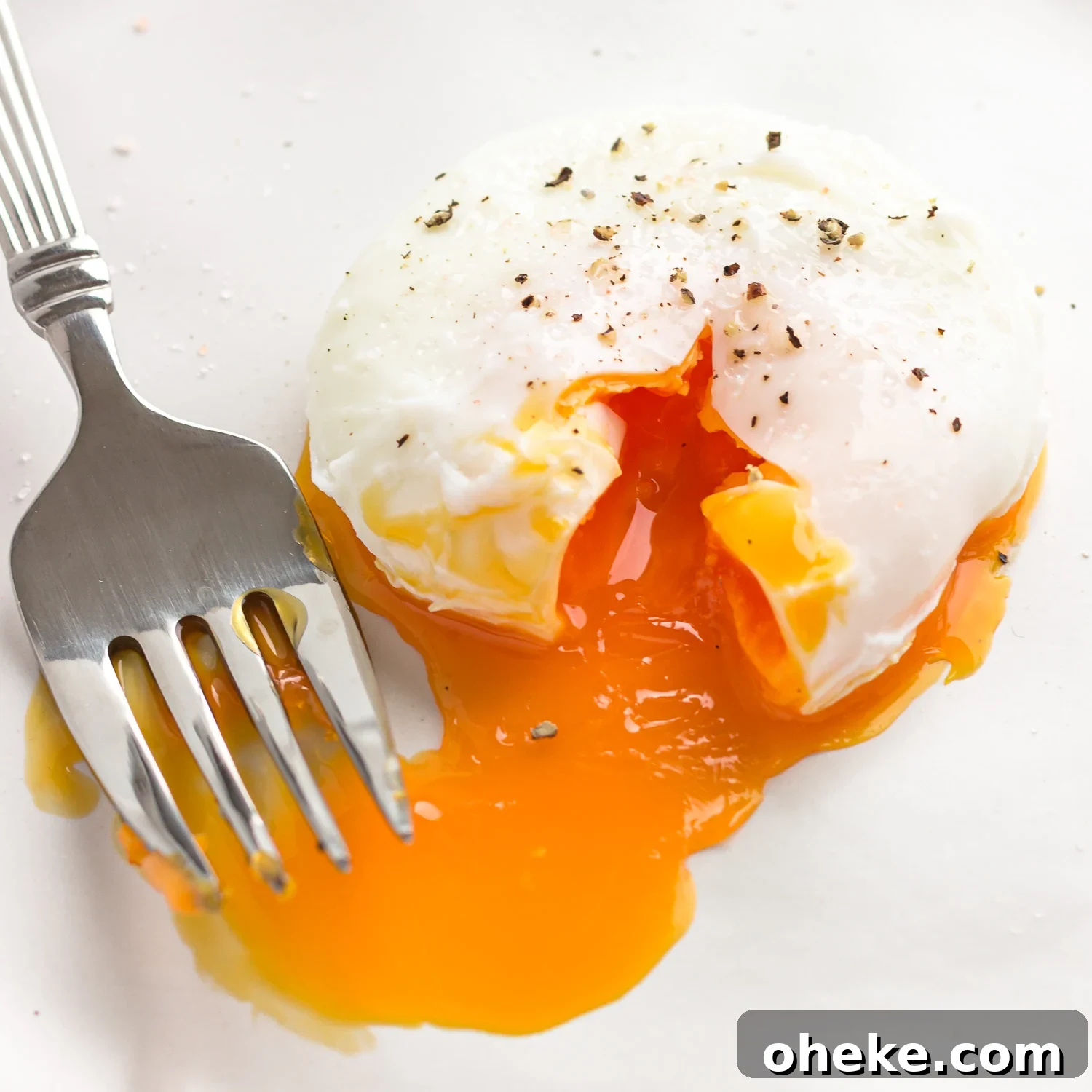 A seasoned poached egg next to a fork with the golden, oozy yolk running out.
