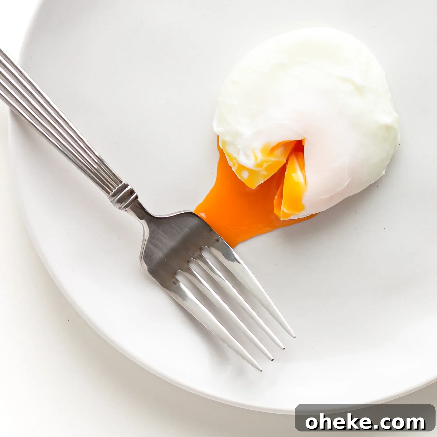 A single poached egg with some yolk oozing out on a white plate with a fork.